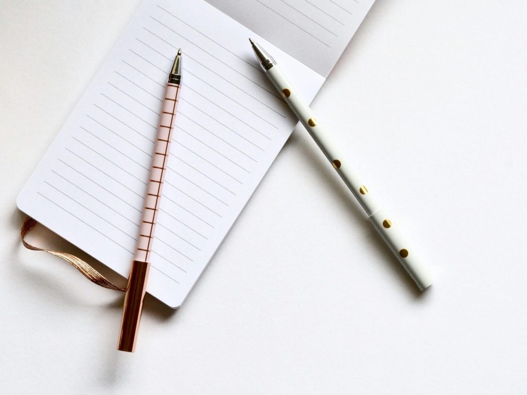 Flat lay of a notepad with two decorative pens on a white surface, ideal for stationery themes.